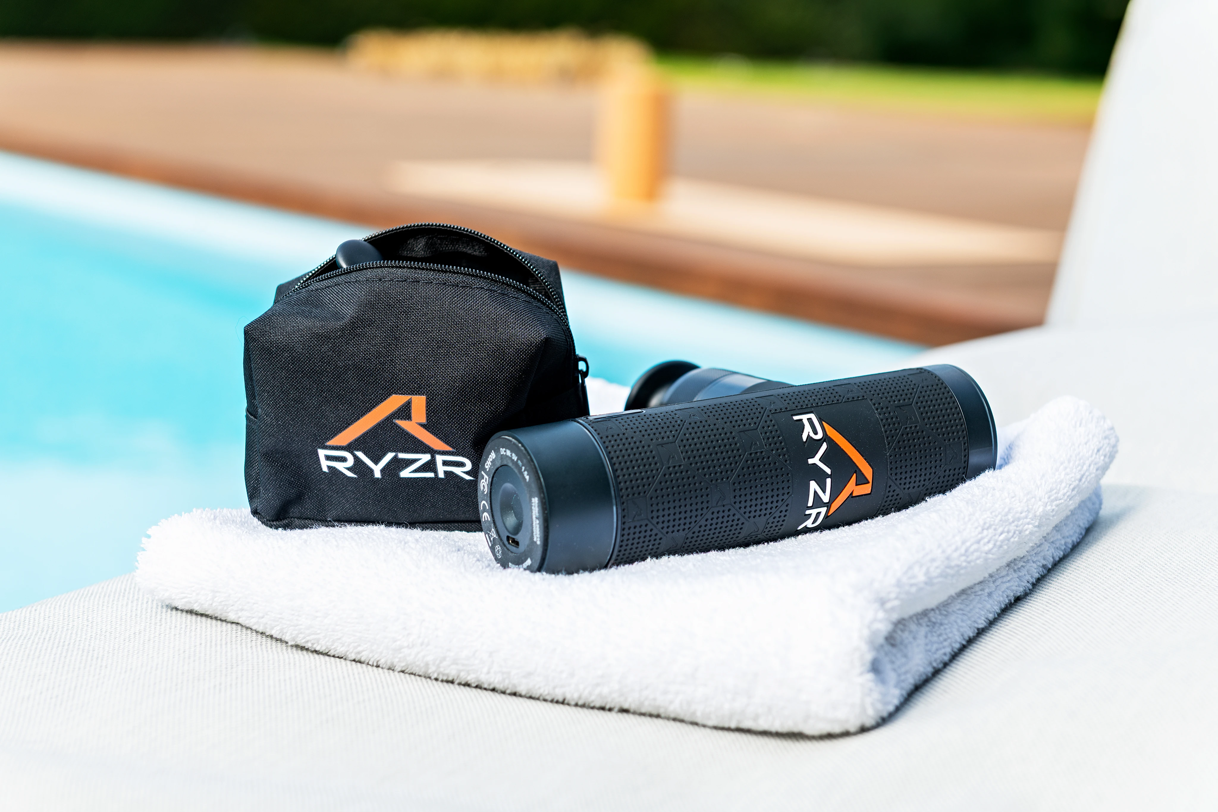 Massagepistole RYZR Minigun mit Transporttasche auf einem Handtuch (Outdoor)